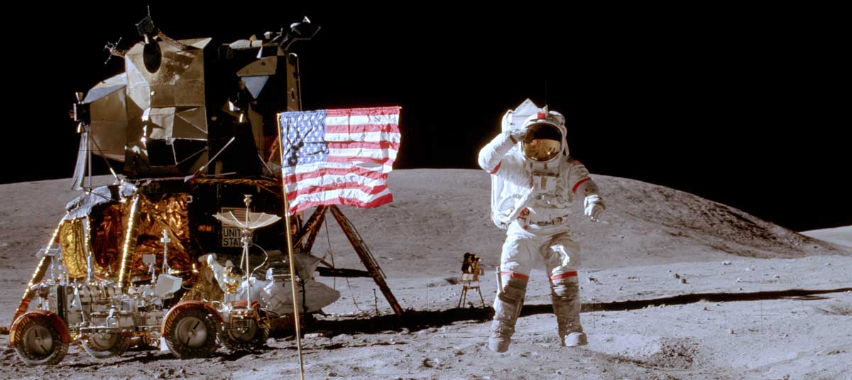 An astronaut standing next to the American flag and the Apollo lander on the Moon.